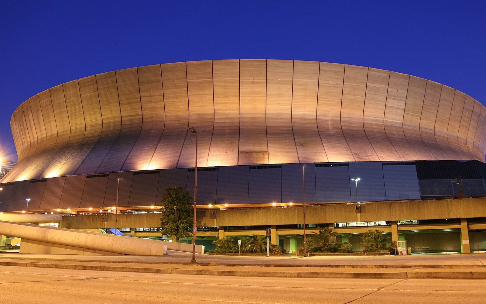 Domed stadium exterior illuminated at dusk beneath a deep blue sky